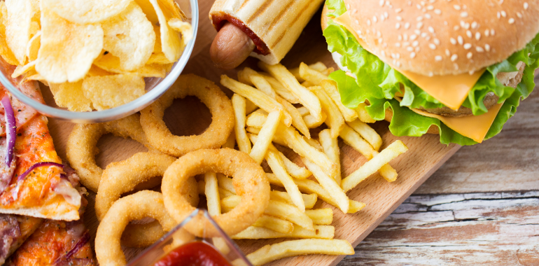Fast food and unhealthy eating concept - close up of hamburger or cheeseburger, deep-fried squid rings, french fries hotdog and potato chips on wooden table top view